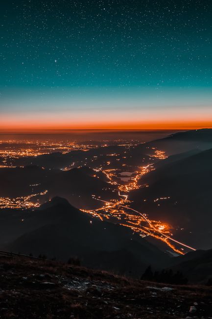 A breathtaking view of a city lit up beneath a starry sky with distant mountains and glowing horizon.
