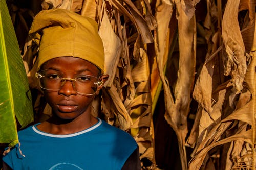 A young boy in a yellow hat and glasses stands in front of a corn field