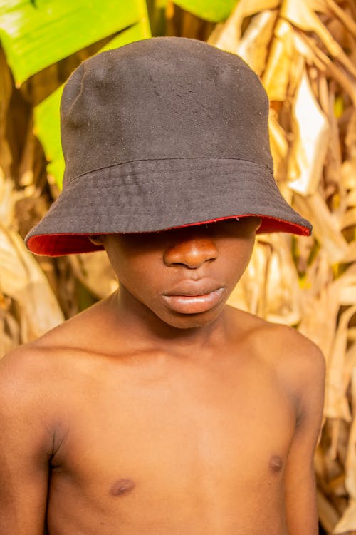A young boy wearing a hat and standing in front of a corn field