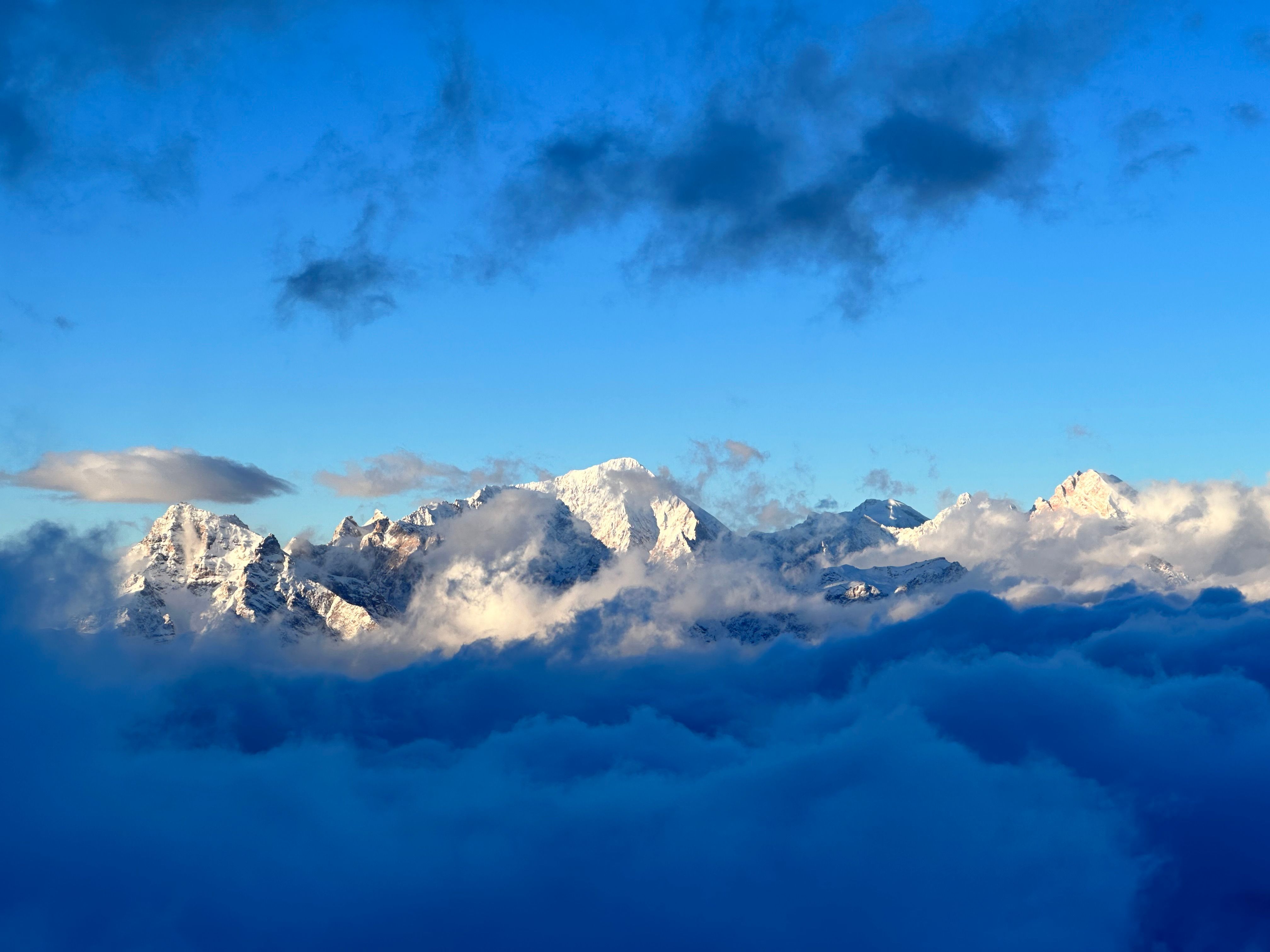 Makalu Expedition - Stunning view of snow-covered mountains rising through fluffy clouds under a vibrant blue sky.