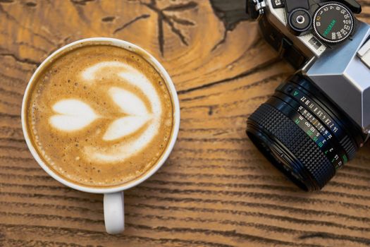 Close-up of a cappuccino with latte art next to a vintage camera on a wooden surface.