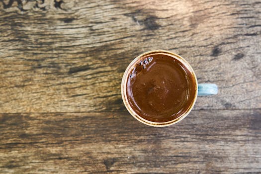 A top view of a mug filled with rich, frothy Turkish coffee on a wooden surface.