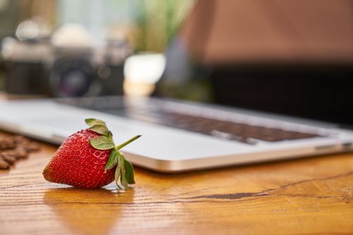 Free Close-up of a fresh strawberry on a wooden table with a laptop and camera in the background. Stock Photo