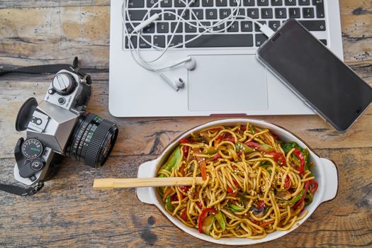 Flat lay of noodles, camera, and laptop on a rustic table. Perfect mix of tech and cuisine for a modern lifestyle.