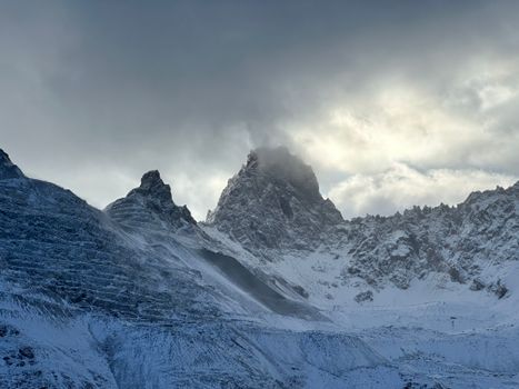 Dramatic mountain peaks covered in snow under a moody, cloudy sky, showcasing winter's beauty.