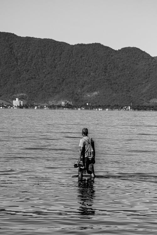 Free Black and white photo of a man standing in water looking at hills, Caraguatatuba. Stock Photo