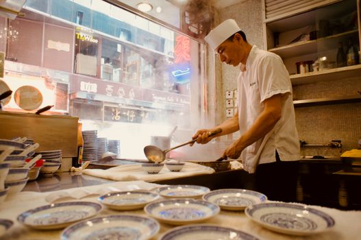 Asian chef in white attire cooking in a bustling Hong Kong restaurant kitchen with steam rising.