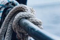 Detailed view of a thick knotted rope wrapped around a metal railing, evoking nautical themes.