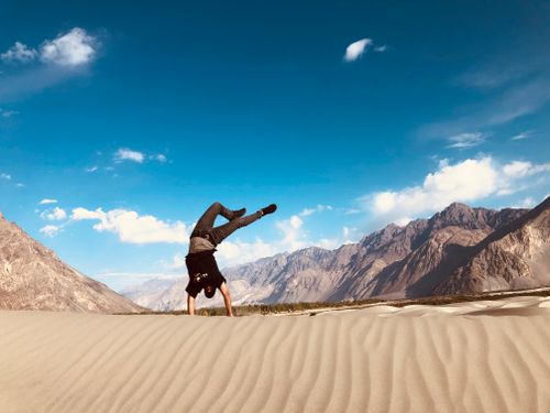 Free A man performing a handstand on the stunning sand dunes of Diskit with mountain scenery. Stock Photo