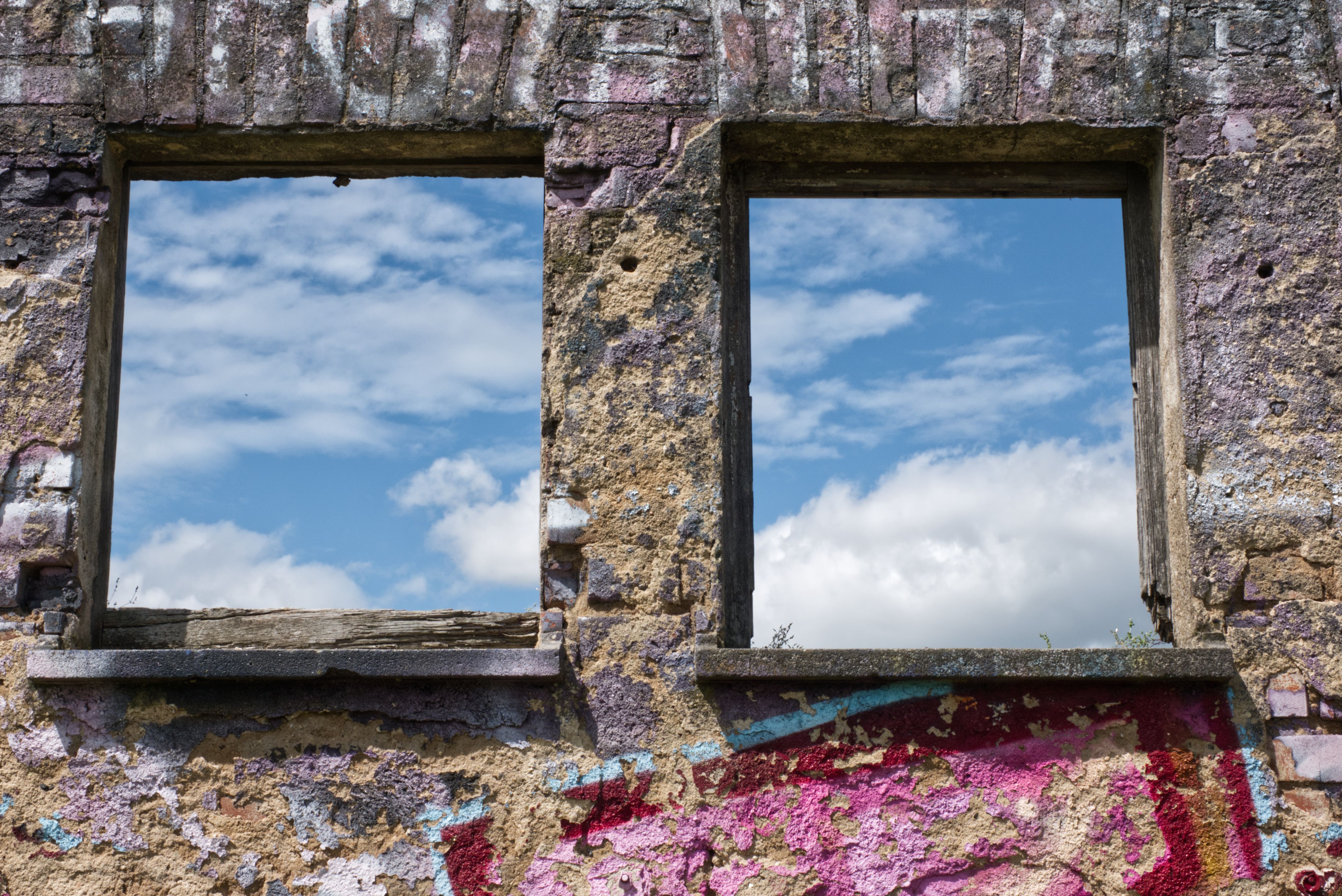 Rustic wall with empty window frames and blue sky view, featuring graffiti art.