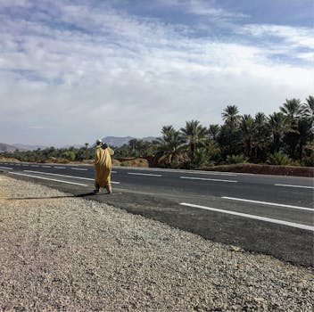 在摩洛哥乌利德奥特马内，一名身着传统服装的男子走在棕榈树掩映的道路上