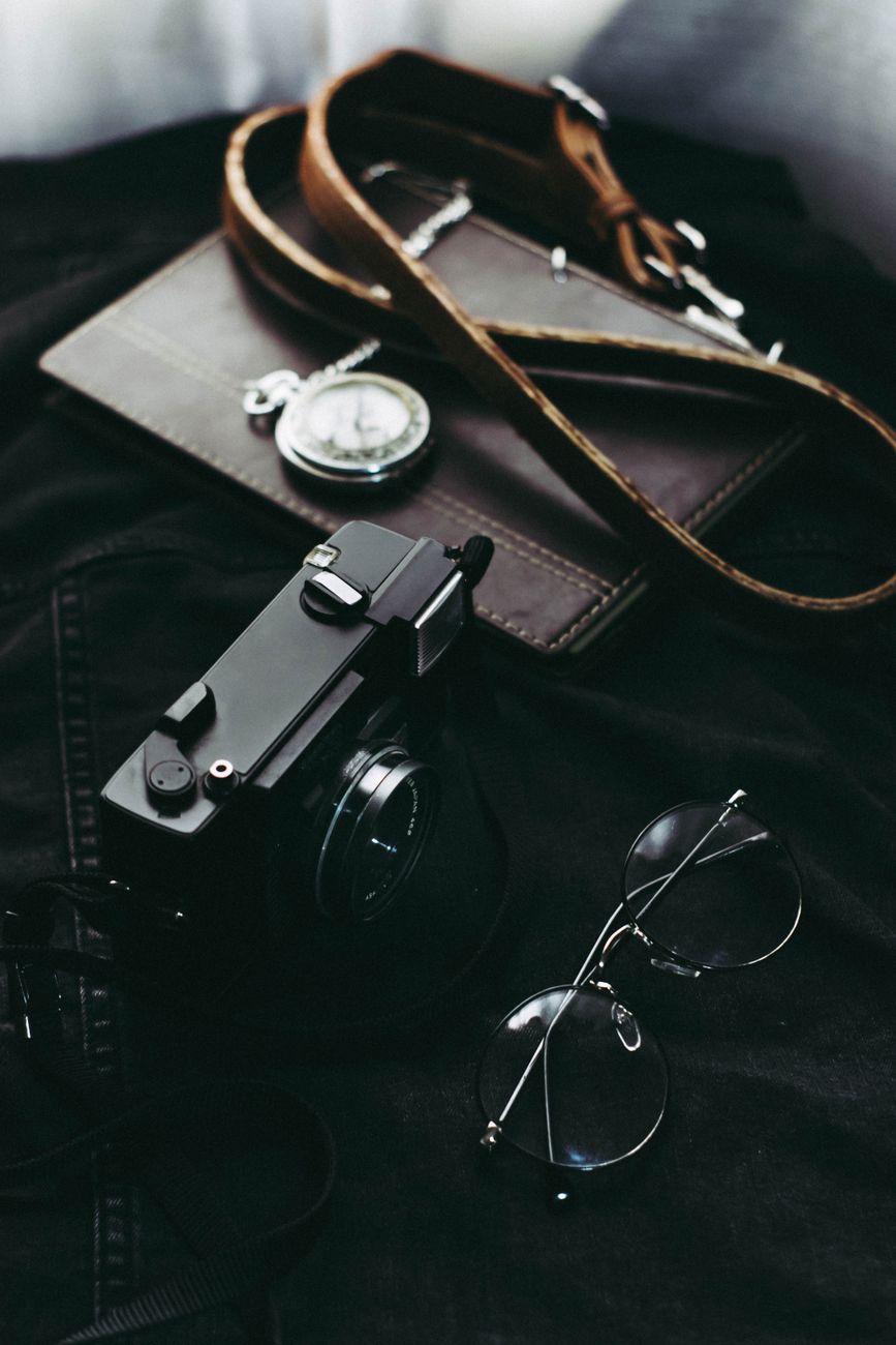 A stylish flat lay of a vintage camera, eyeglasses, and leather accessories.