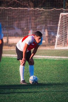 A tired soccer player resting on the field, showing fatigue and determination in a sports match.