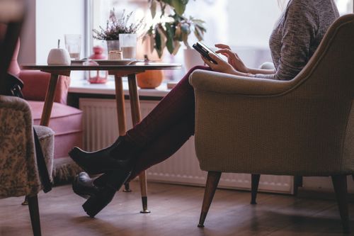 Free Woman in cozy setting seated with smartphone, wearing stylish boots and jeans. Stock Photo