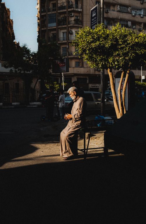 Free An elderly man sits thoughtfully on a street in Cairo, Egypt, captured in beautiful backlit sunlight. Stock Photo
