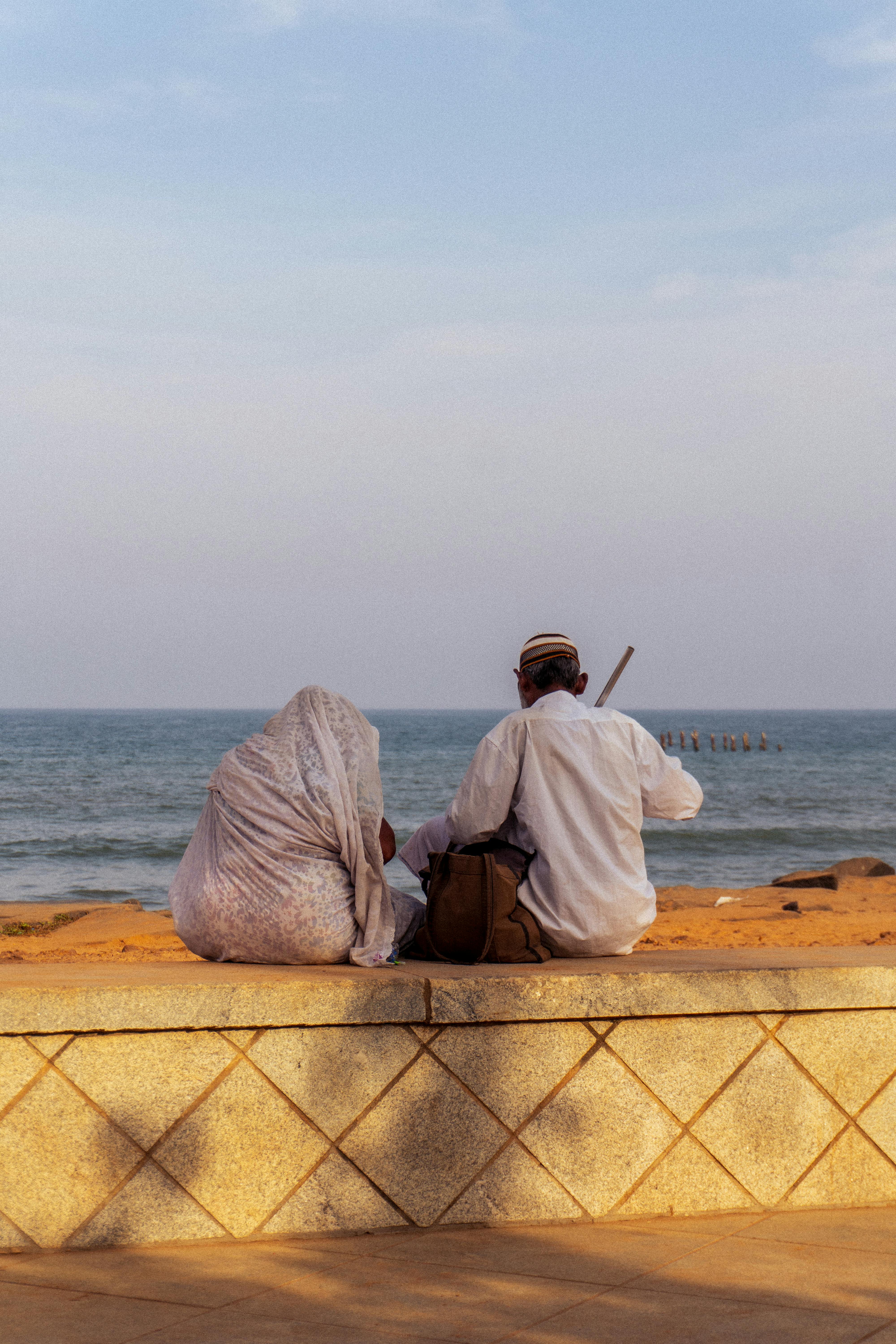 A couple sits by the seashore in Puducherry, India, enjoying a serene ocean view at sunset.