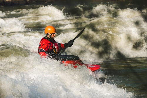 Free Man kayaking through whitewater rapids, showcasing adventure and outdoor excitement. Stock Photo