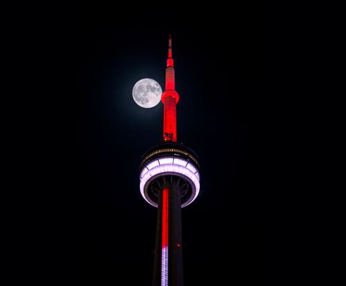 Free Iconic CN Tower lit up in red with a full moon in Toronto's night sky. Stock Photo
