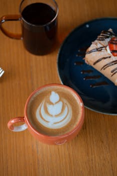 Close-up view of a cappuccino with latte art and dessert on a table, creating a cozy coffee shop vibe.