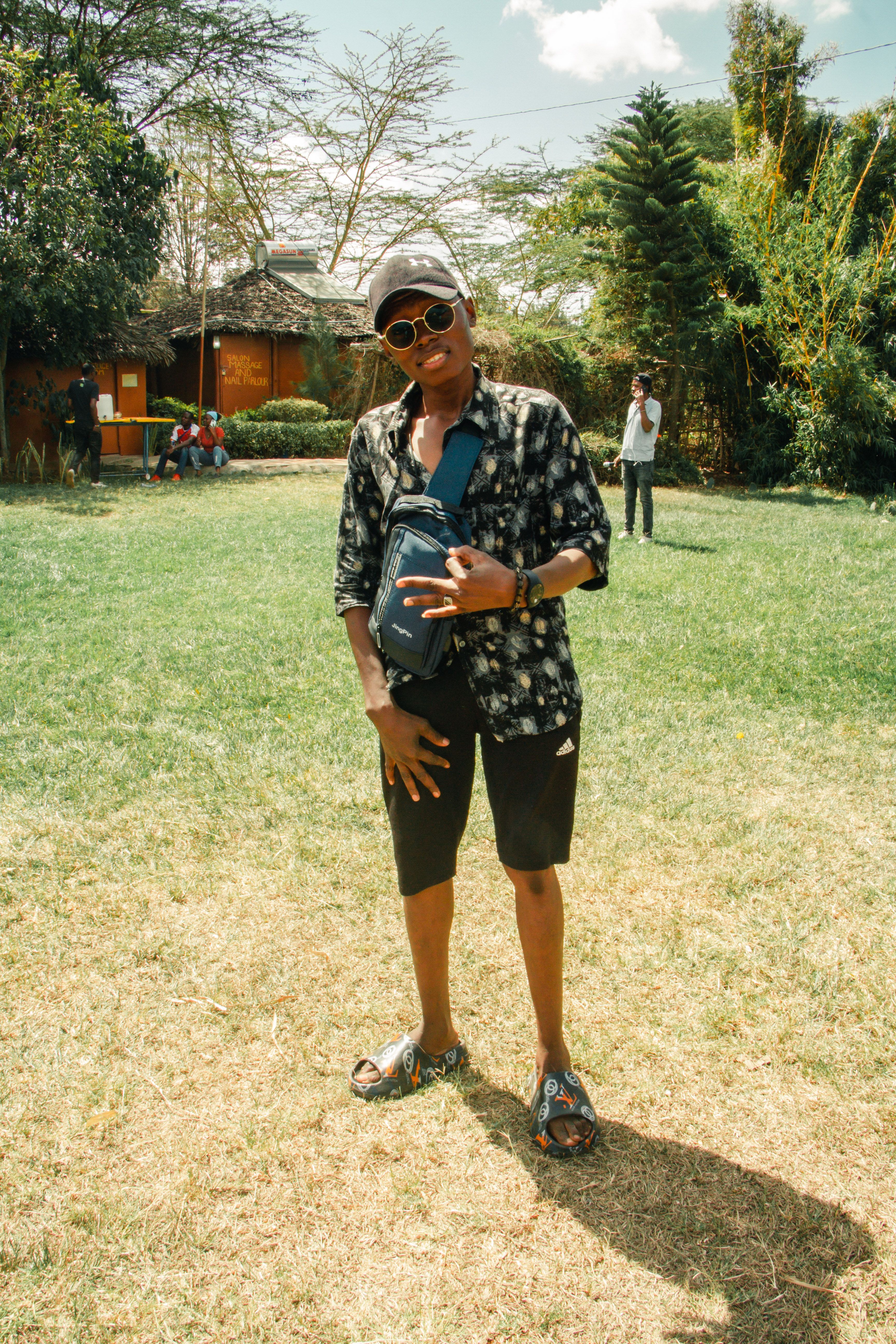 Casual portrait of a young man wearing sunglasses in a sunny garden setting.