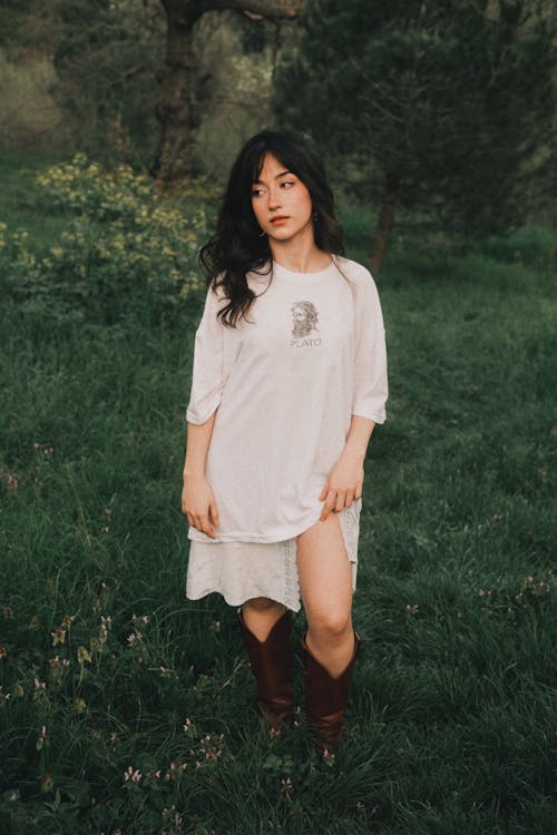 A woman in a white shirt and boots standing in a field