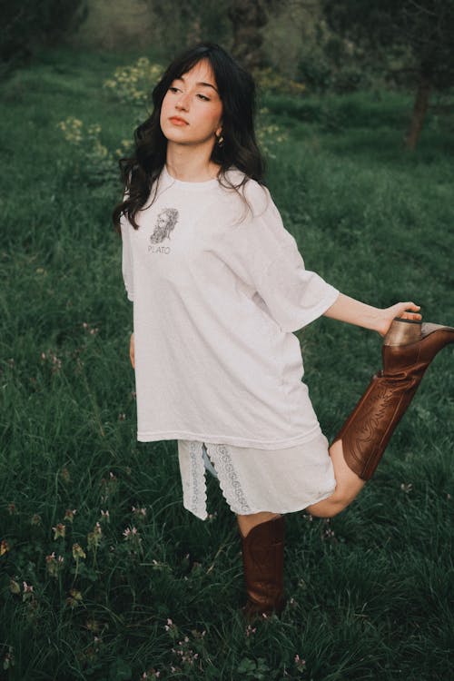 A woman in a white shirt and brown boots standing in a field