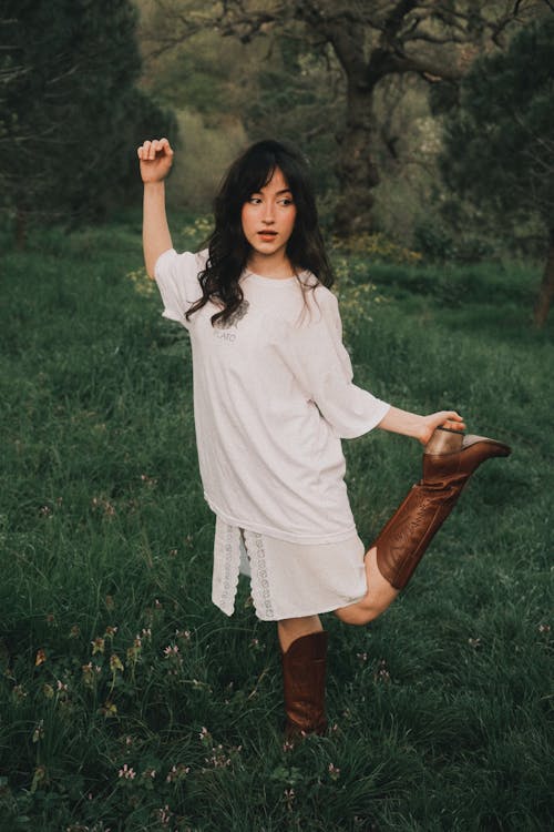 A woman in a white shirt and brown boots is posing in a field