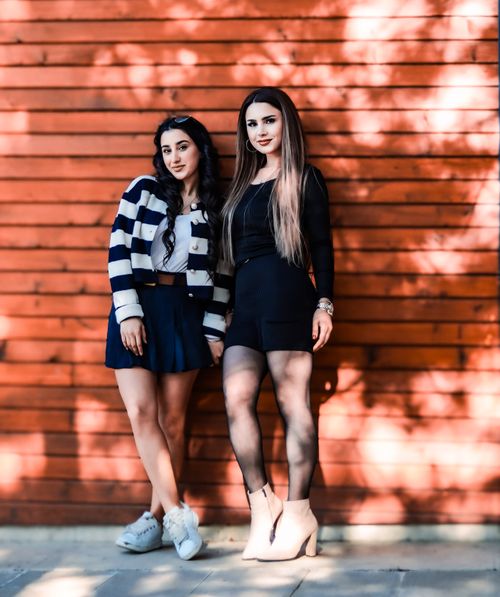 Free Two fashionable young women standing against a wooden wall, showcasing stylish outfits. Stock Photo