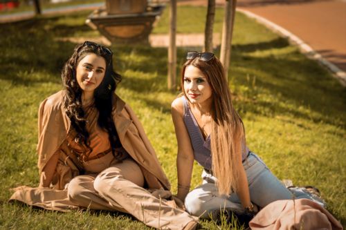 Free Two fashionably dressed women sitting on a grassy lawn enjoying the outdoors on a sunny day. Stock Photo