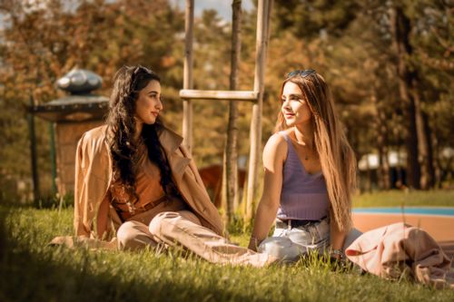 Free Two young women enjoying a sunny day sitting on grass in a park, smiling and at leisure. Stock Photo