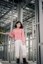 在都市工业环境中，一位穿着粉红色上衣和白色裤子的时髦妇女