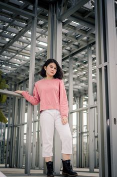在都市工业环境中，一位穿着粉红色上衣和白色裤子的时髦妇女
