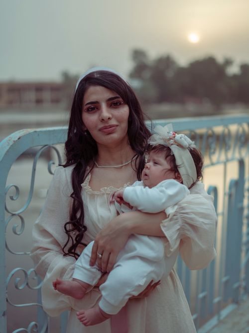Free A woman holding her baby on a Baghdad bridge at sunset, expressing warmth and connection. Stock Photo
