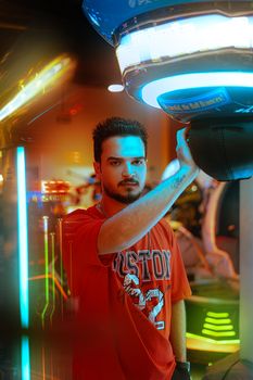 Young man in a t-shirt enjoying a vibrant arcade center with neon lights.