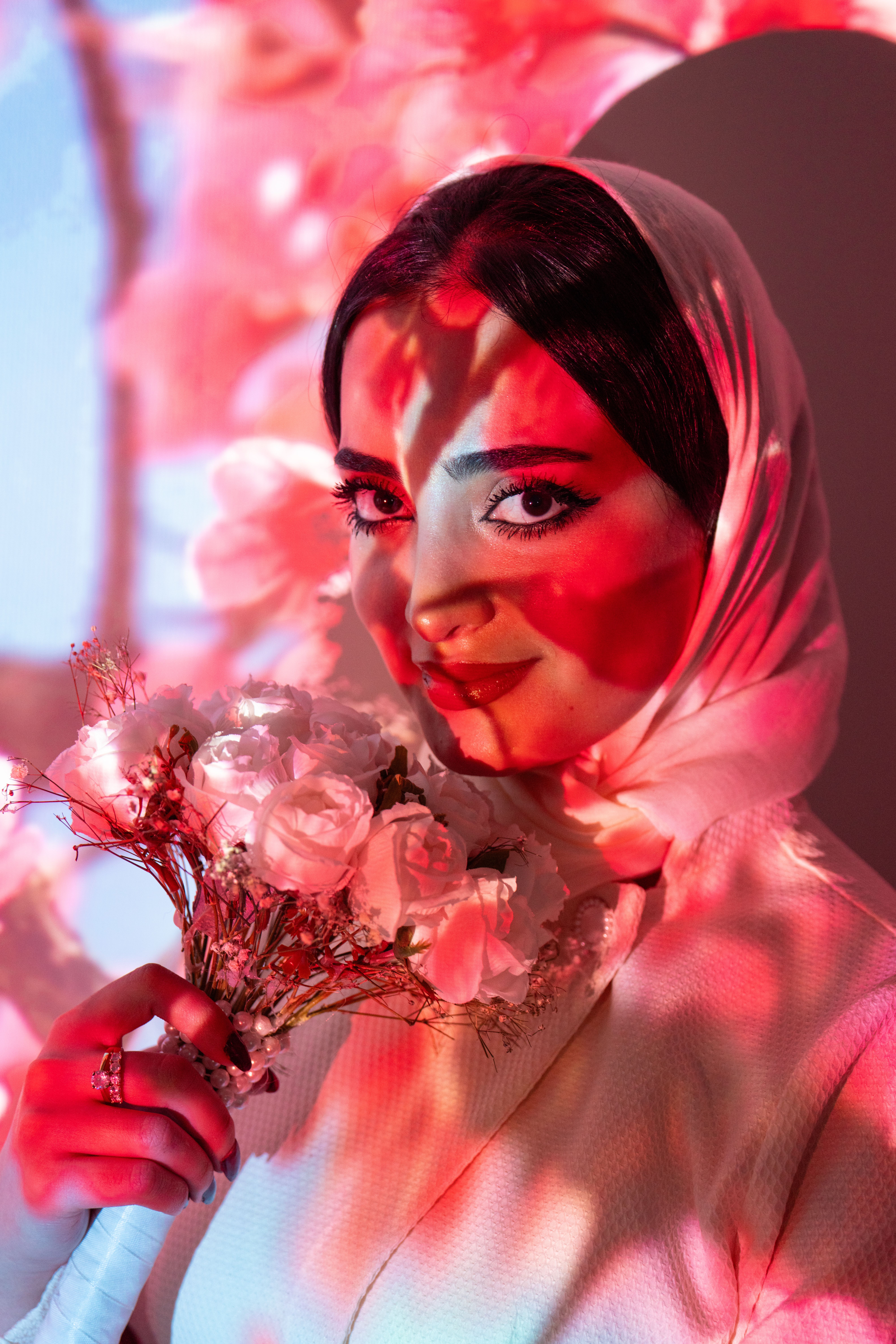 Portrait of a woman in hijab holding flowers under red light. Striking and elegant.
