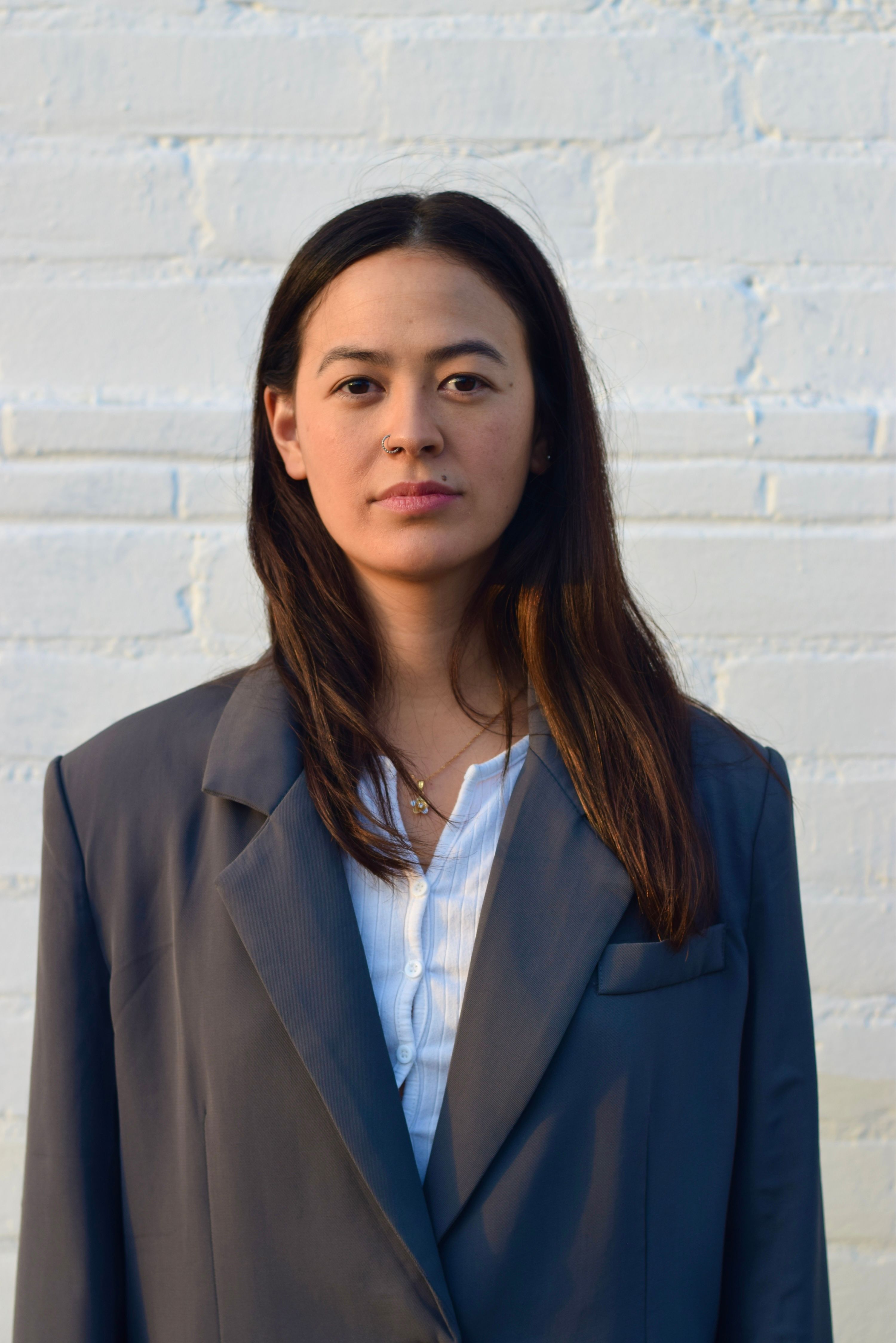 Asian woman modeling oversized business jacket against a white brick wall in Los Angeles.