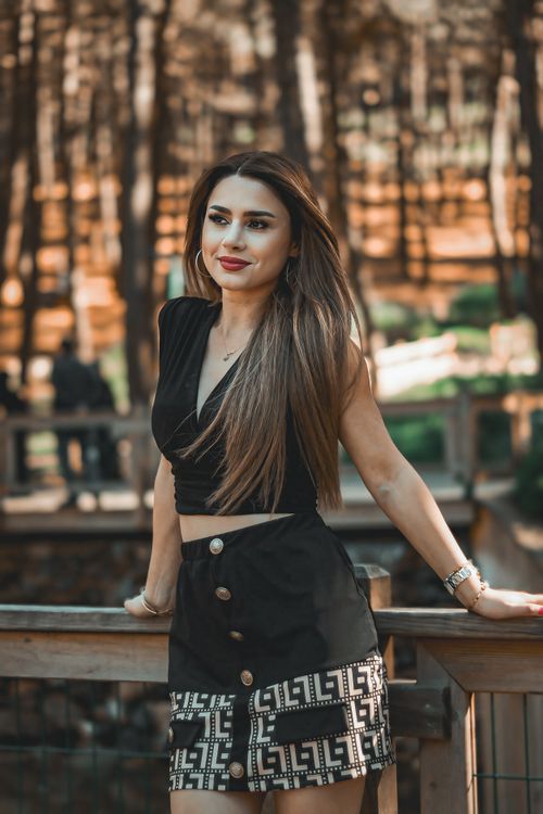 Free Elegant woman with long hair posing outdoors by wooden railing in forest setting. Stock Photo
