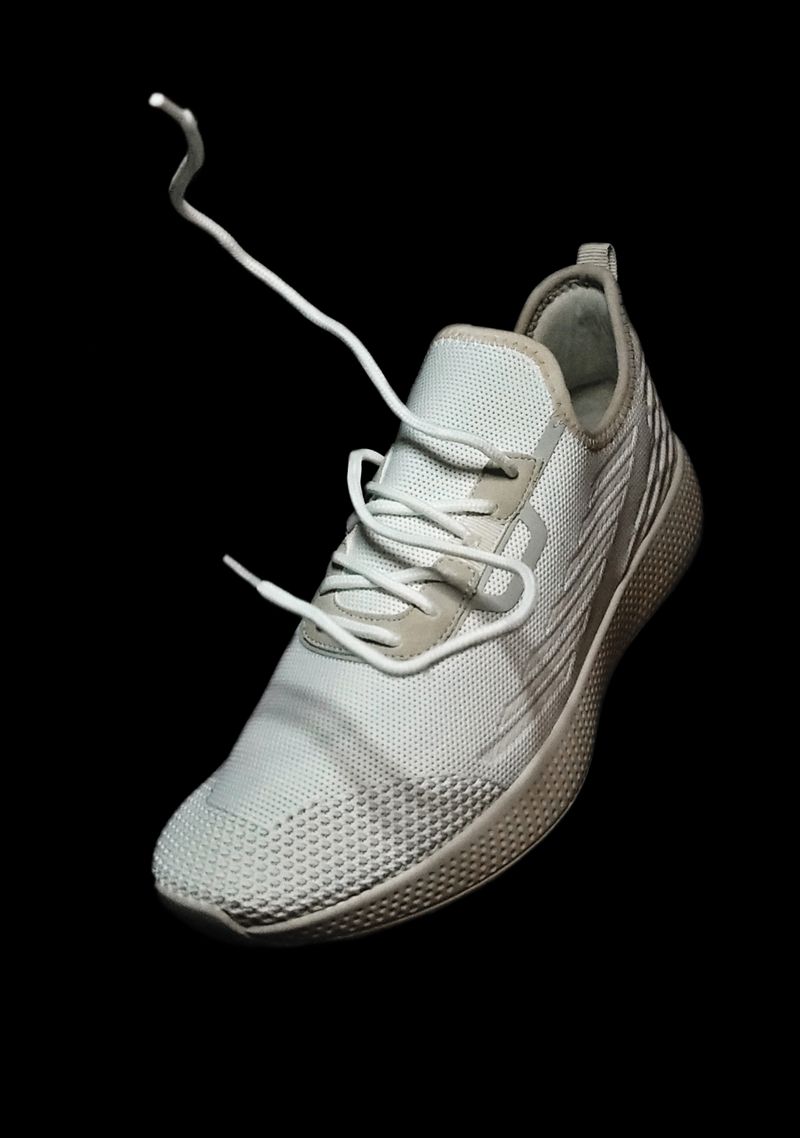 White knit running shoe suspended against black — photo by Pranay Patel on Pexels