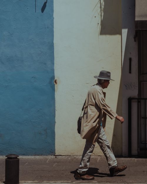 Free An elderly man in a fedora walks past a blue wall on a sunny day in Puebla, Mexico. Stock Photo