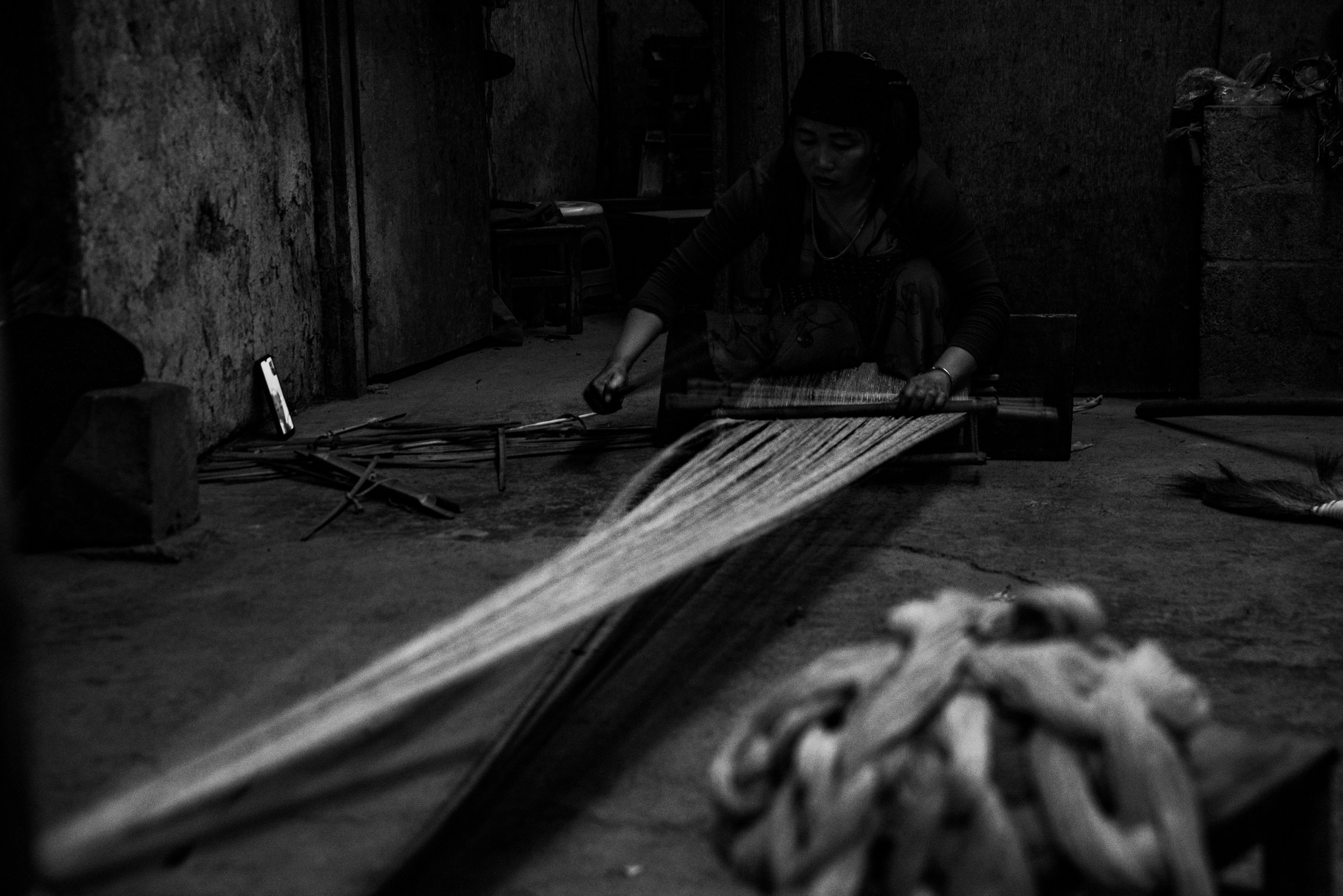 A woman attentively weaves fabric in a traditional artisan setting, highlighting labour and craftsmanship.