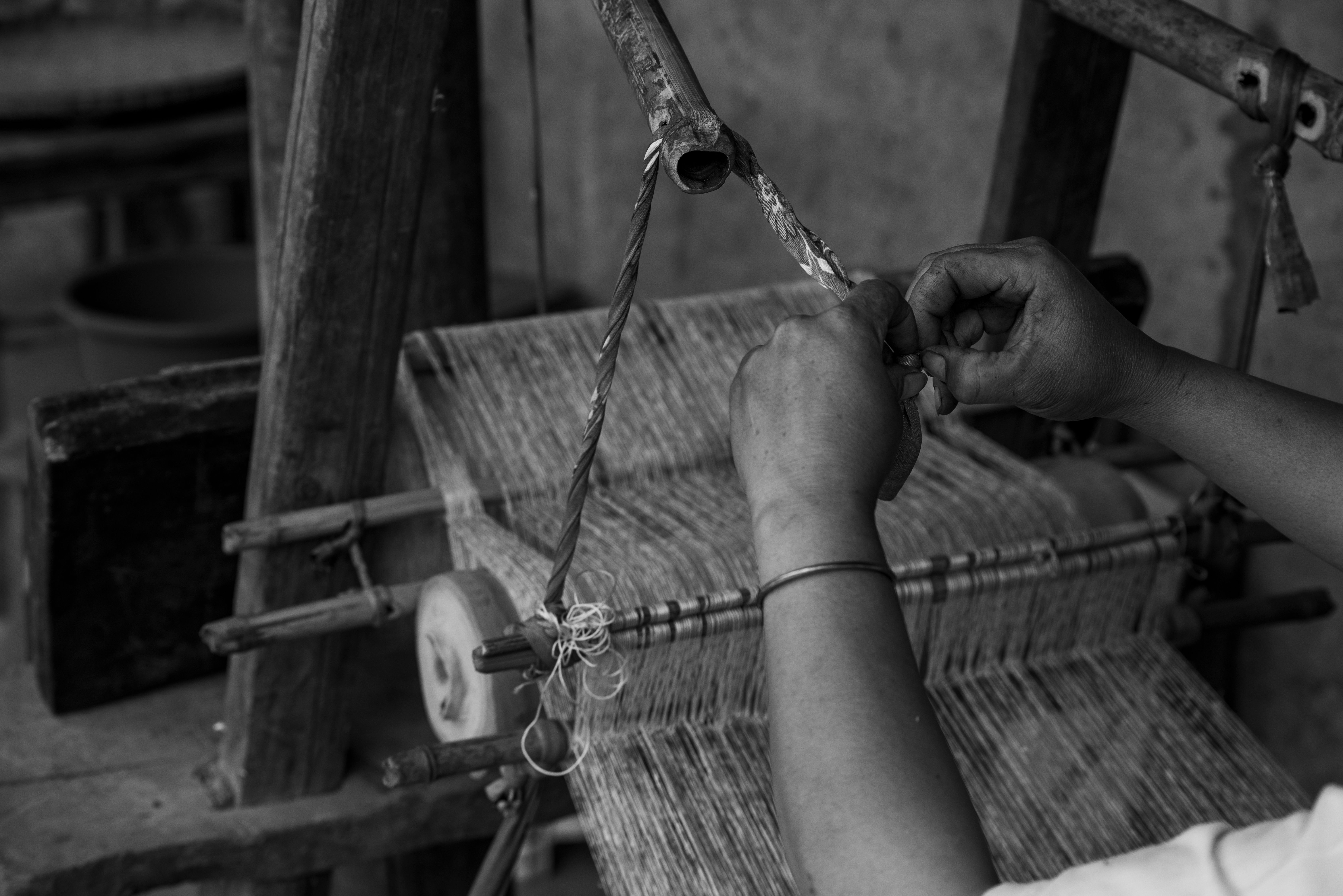 Closeup of hands weaving on a loom in a black and white setting, showcasing traditional craftsmanship.
