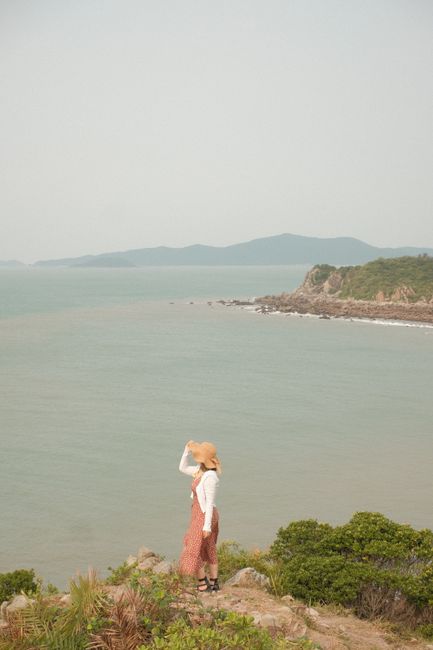 Woman in sun hat enjoying scenic view of coastline in Quảng Ninh, Vietnam with lush greenery.