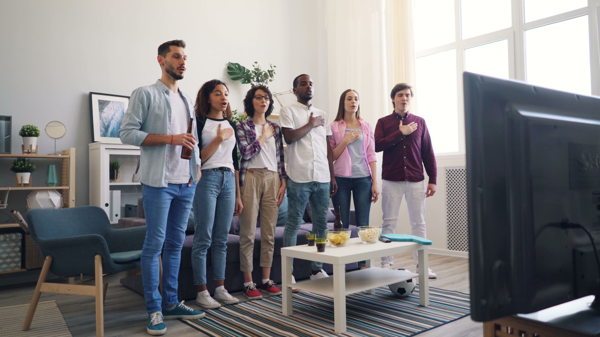 A group of people standing in a living room watching tv