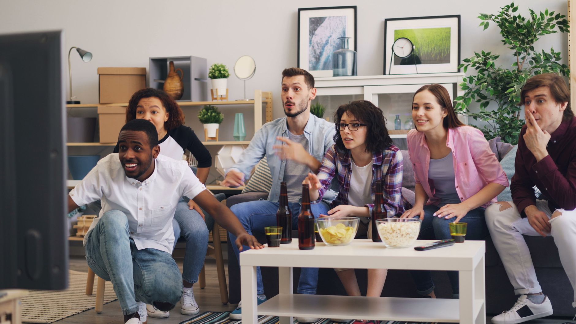 A diverse group of friends excitedly watching TV together in a modern living room setting.