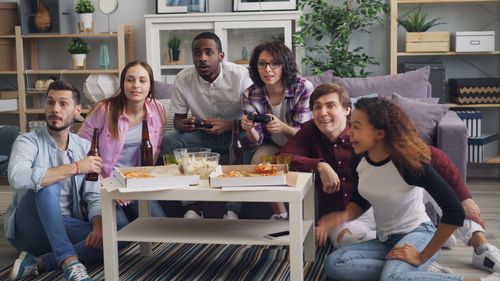 Free A diverse group of friends having fun and playing video games in a cozy living room. Stock Photo
