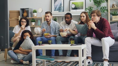 Free Group of friends watching a movie on a couch, enjoying snacks and drinks indoors. Stock Photo