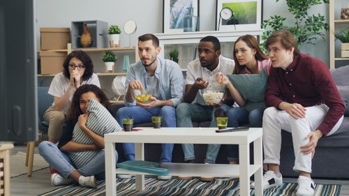Free Group of friends watching a thriller movie at home, sharing snacks and reactions. Stock Photo