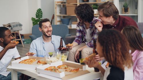 Free Happy friends gathered indoors enjoying pizza and drinks in a relaxed setting. Stock Photo