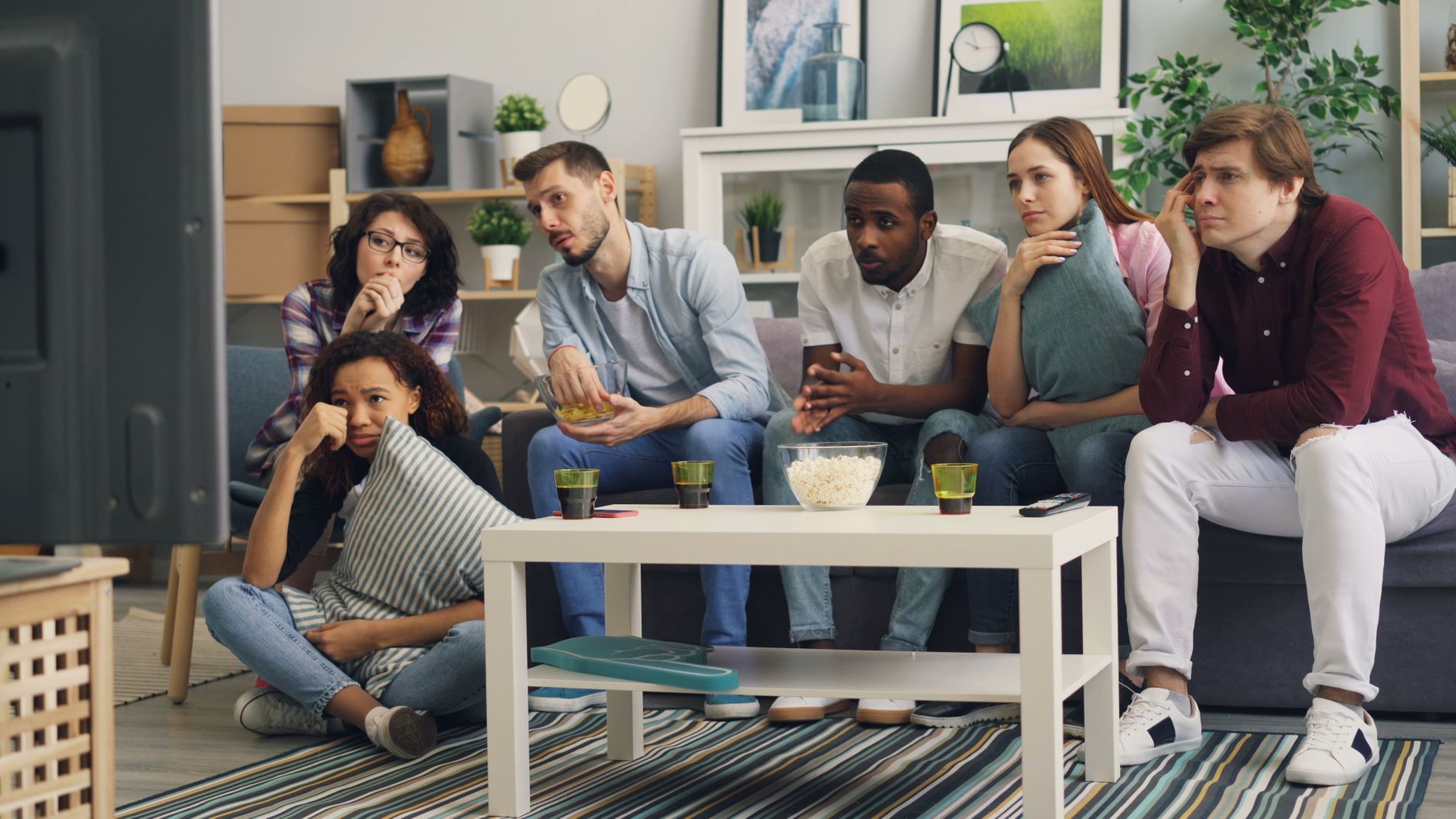 Family watching an Indian drama on JioHotstar television app, subtitles visible, snacks on a wooden table