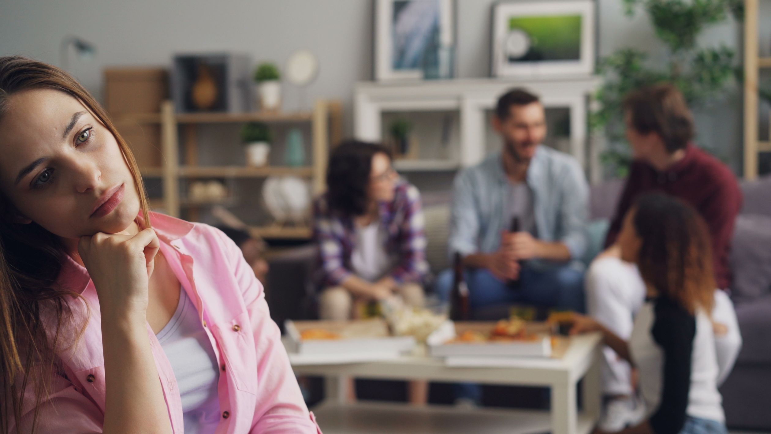 Uma jovem mulher parece solitária em uma festa enquanto outros conversam.
